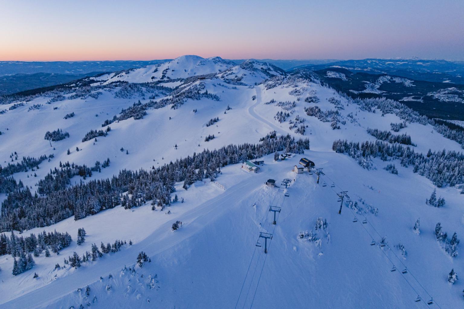 Snow-covered mountain at dawn with ski lifts and pink sky.