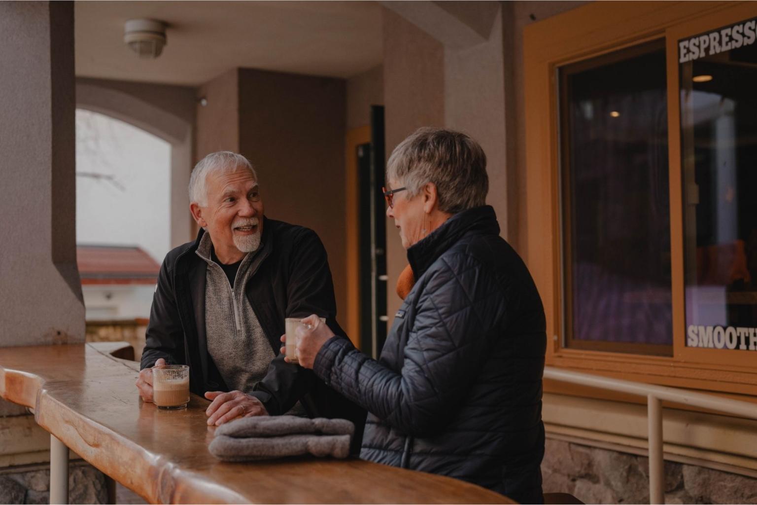 Two people smiling, conversing at an outdoor café table.
