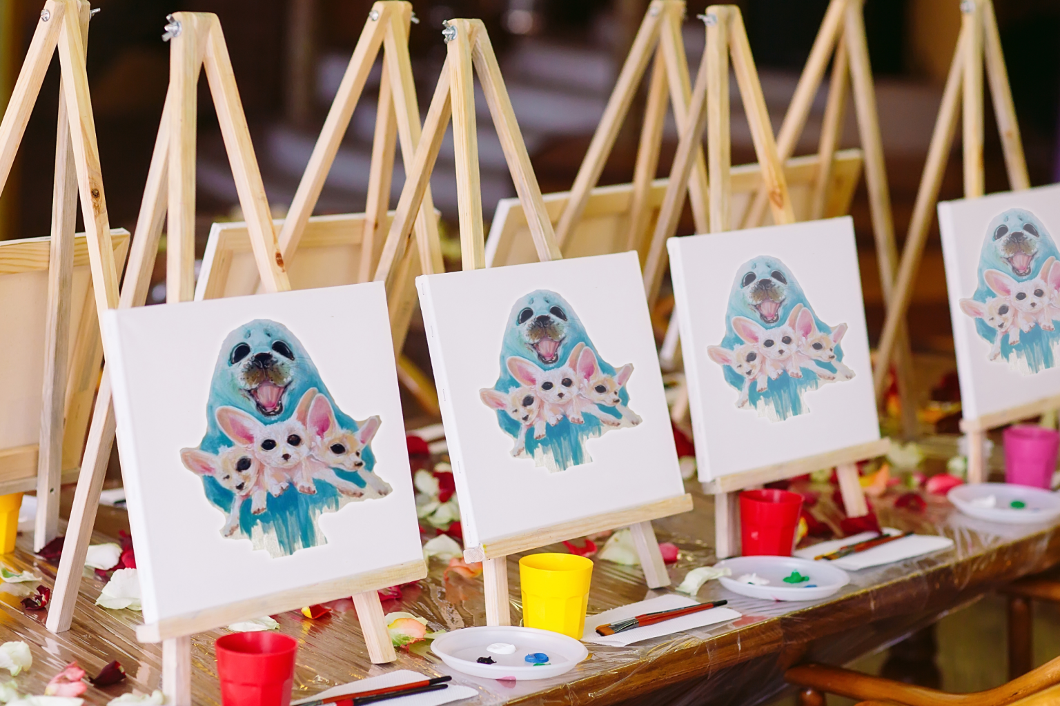 Five easels with identical paintings of a blue mask and flowers, each with paint supplies.