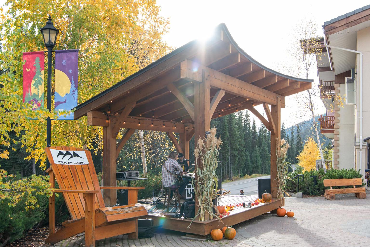 Wooden pavilion with autumn decor, surrounded by trees and pumpkins.