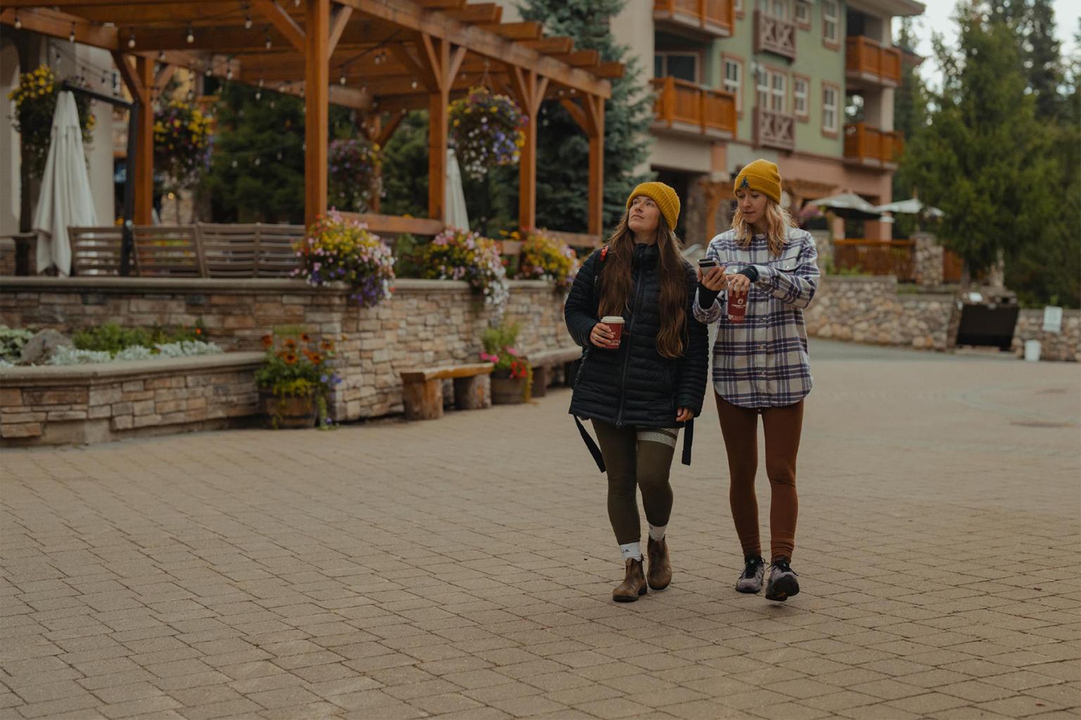 Two people in yellow hats walk in a paved courtyard, surrounded by greenery and buildings.