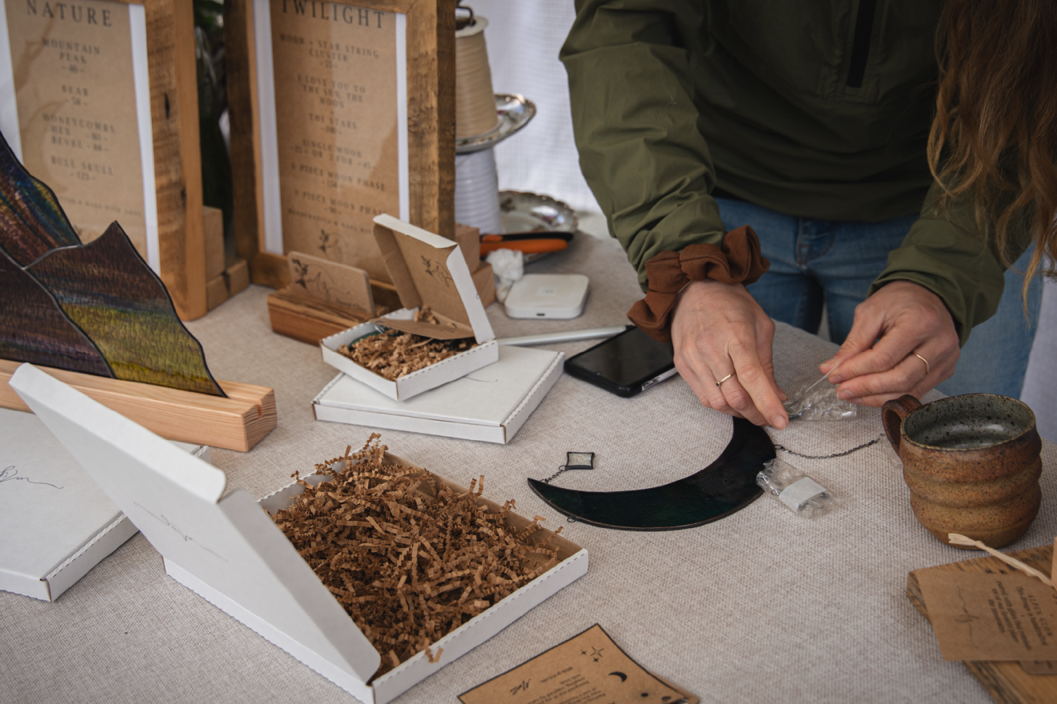 Market stall with jewelry and packaging boxes. A person is arranging items on a table.