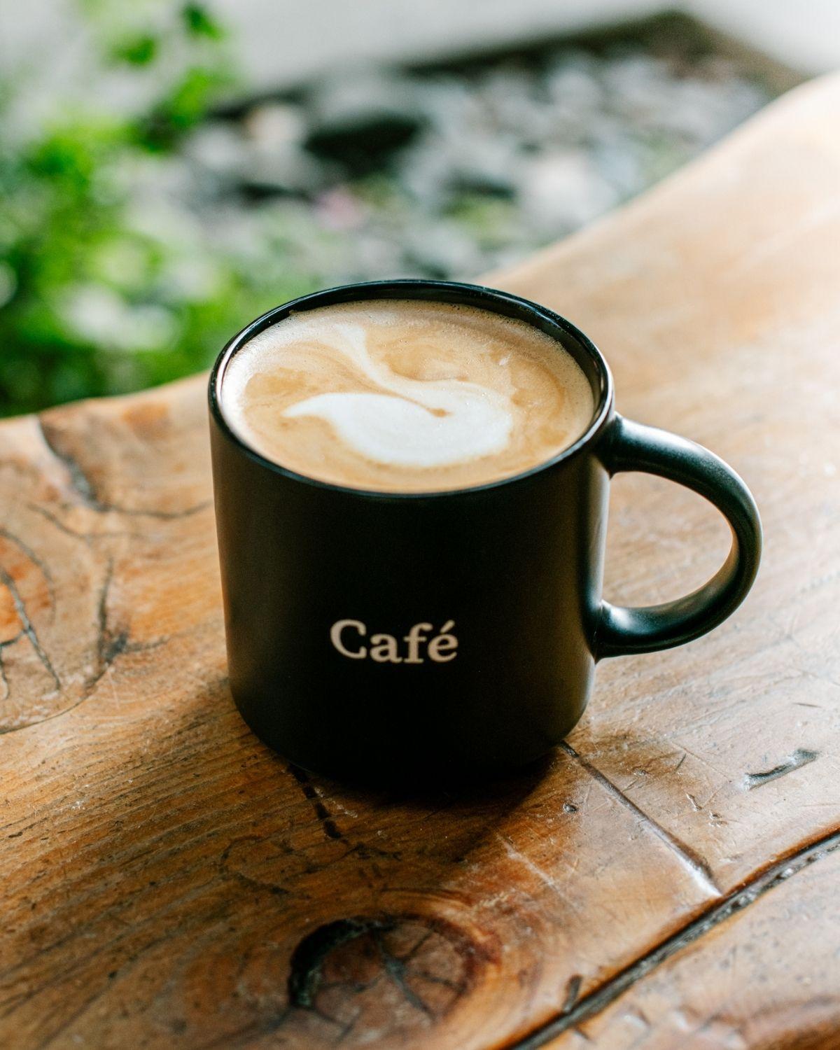 Black mug with latte art on a wooden table.