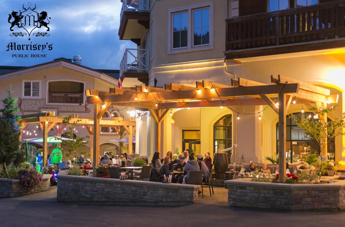 Text: Morrisey's Public House Logo. Restaurant patio with people dining under a wooden pergola, warmly lit at dusk.