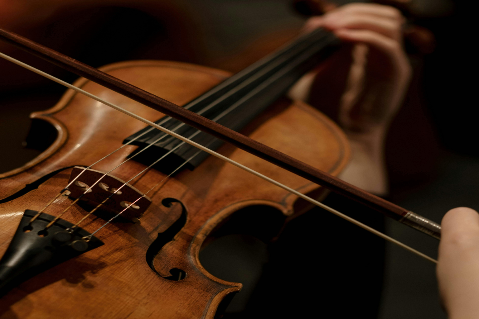 Violin being played with a bow in dim lighting.