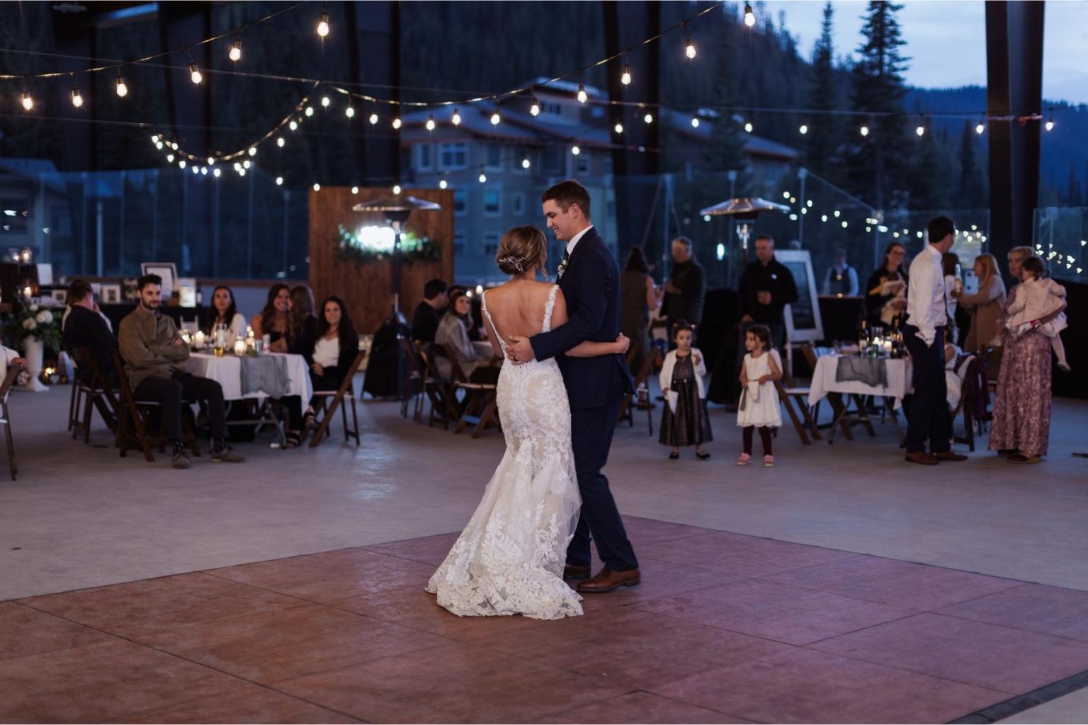 Bride and groom dance under string lights at an outdoor evening wedding reception.