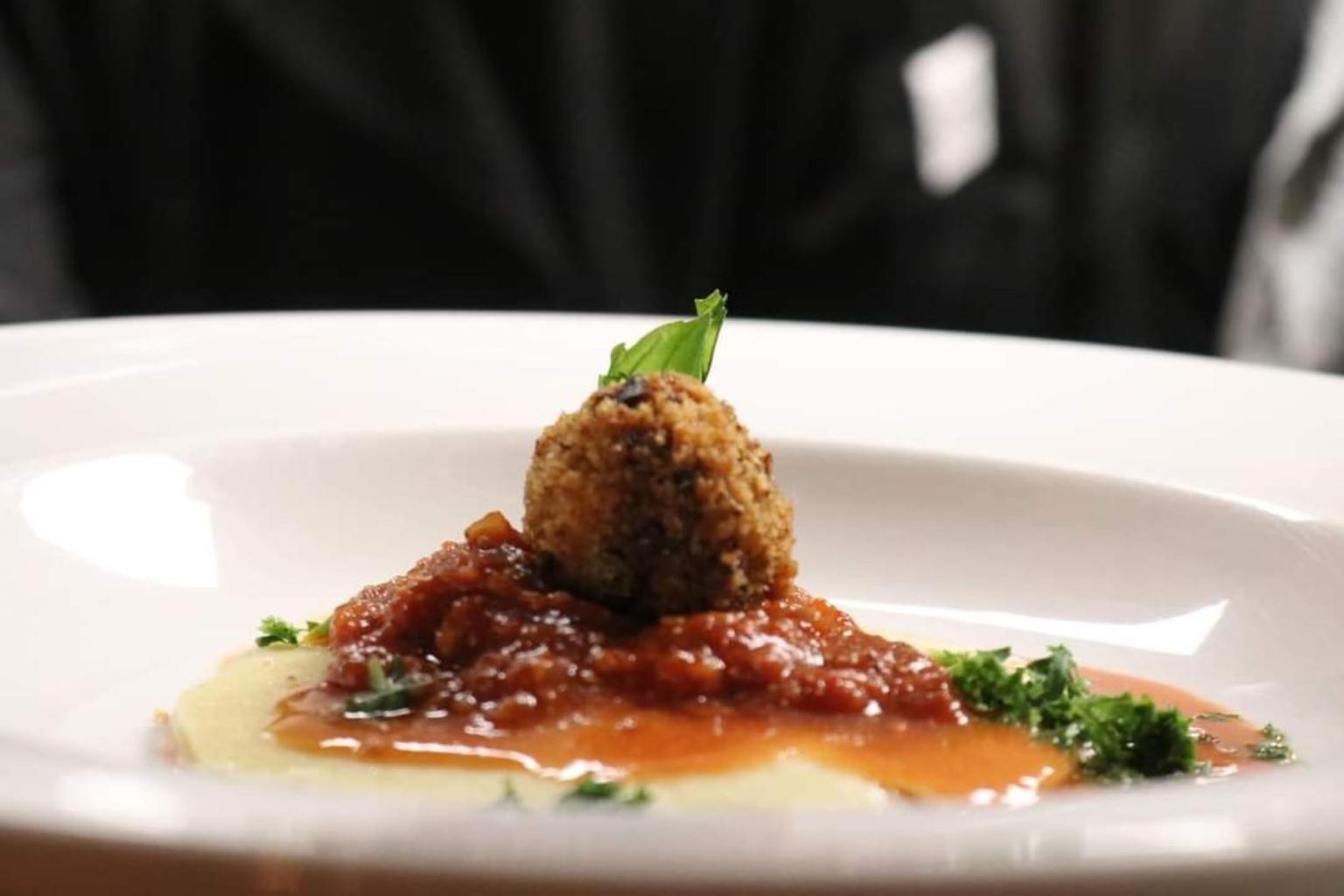 Meatball on pasta with sauce, garnish, served on a white plate.