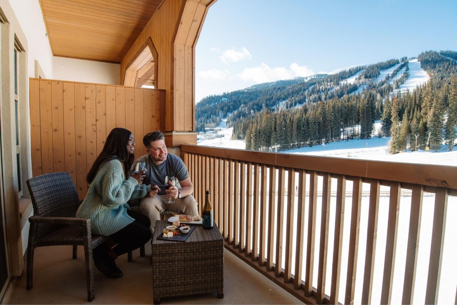 Couple enjoying a meal on a balcony with snowy mountain view.