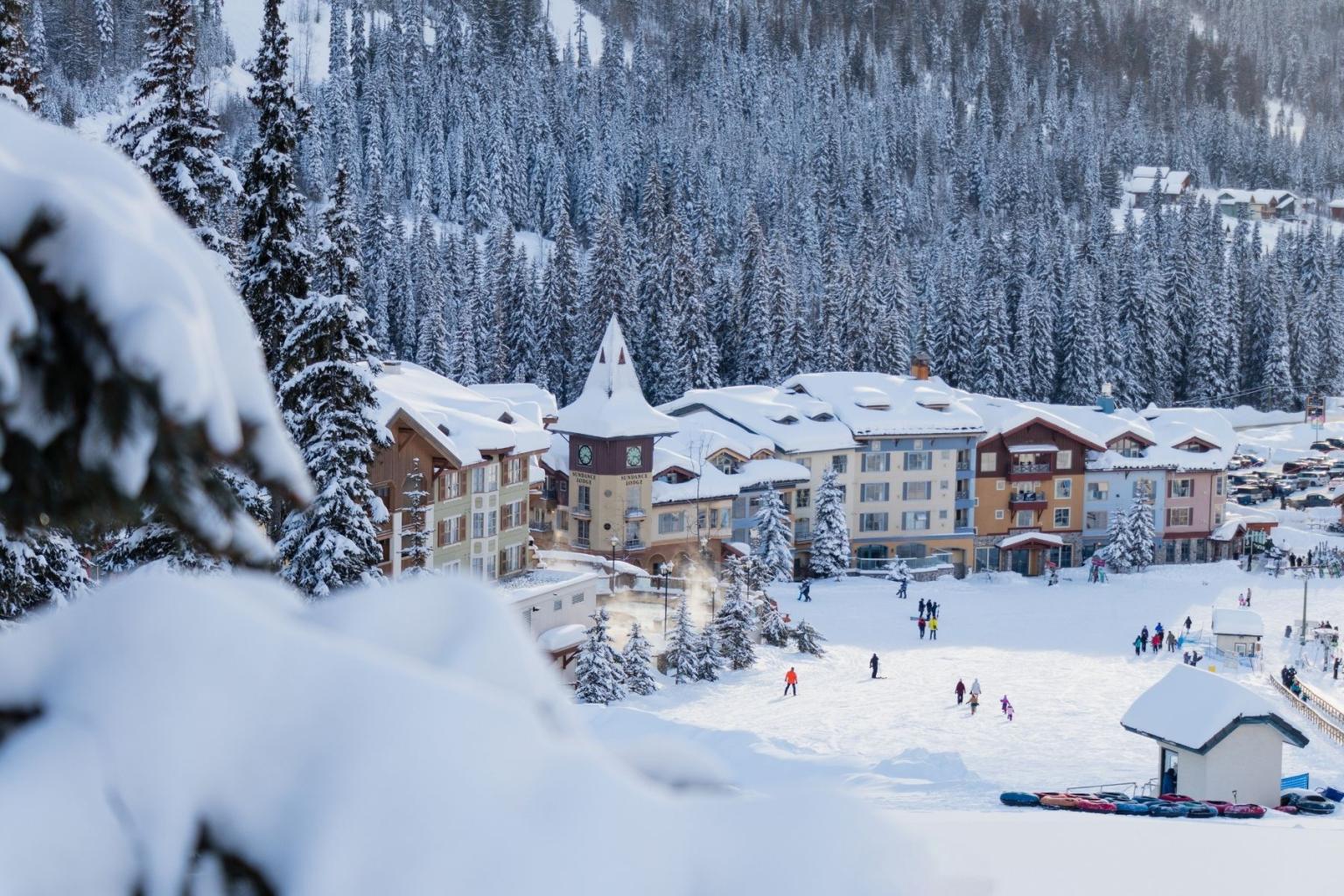 Snowy village with colorful buildings, skiers, and snow-covered trees in the background.