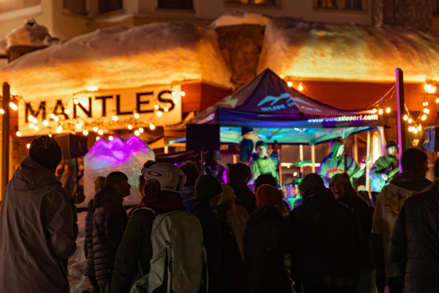 Crowd watching an outdoor musical performance under colorful lights at night.