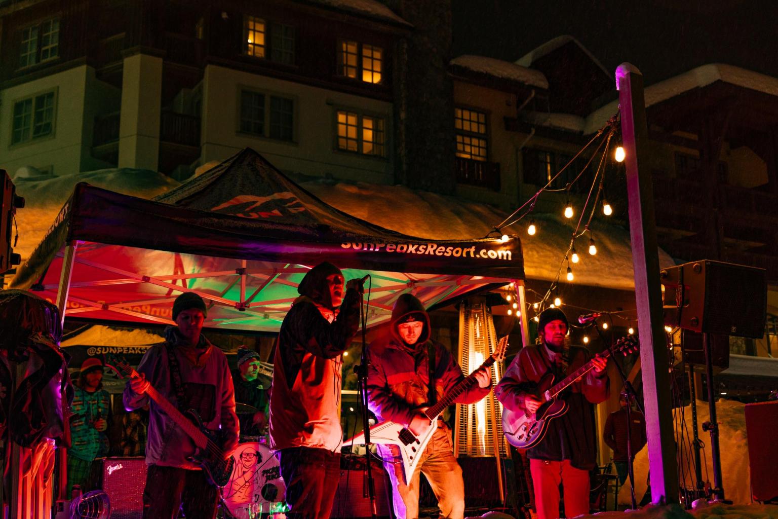 Band performing under colorful lights at an outdoor night venue.