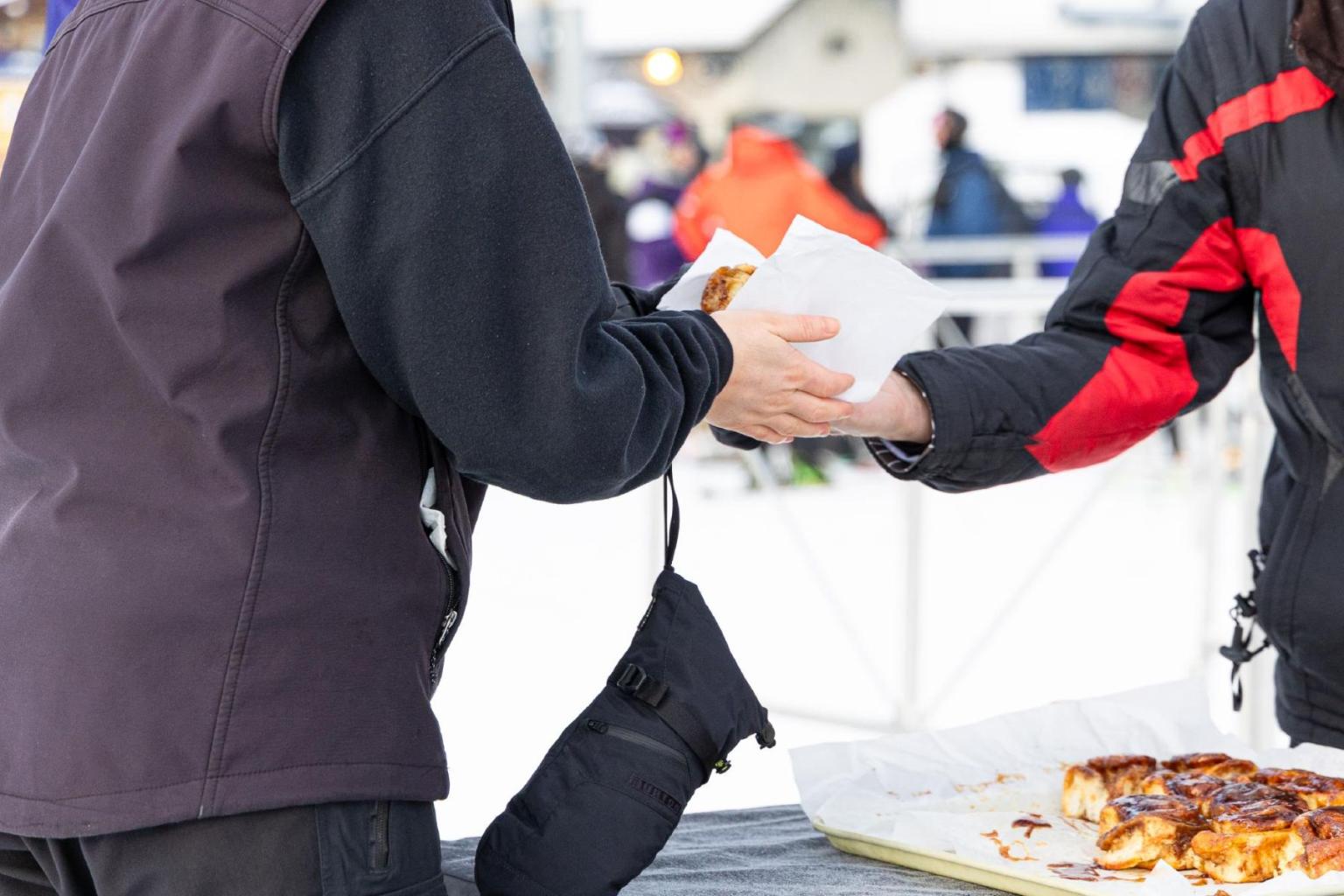 Exchange of cinnamon bun at an outdoor table in the snow.