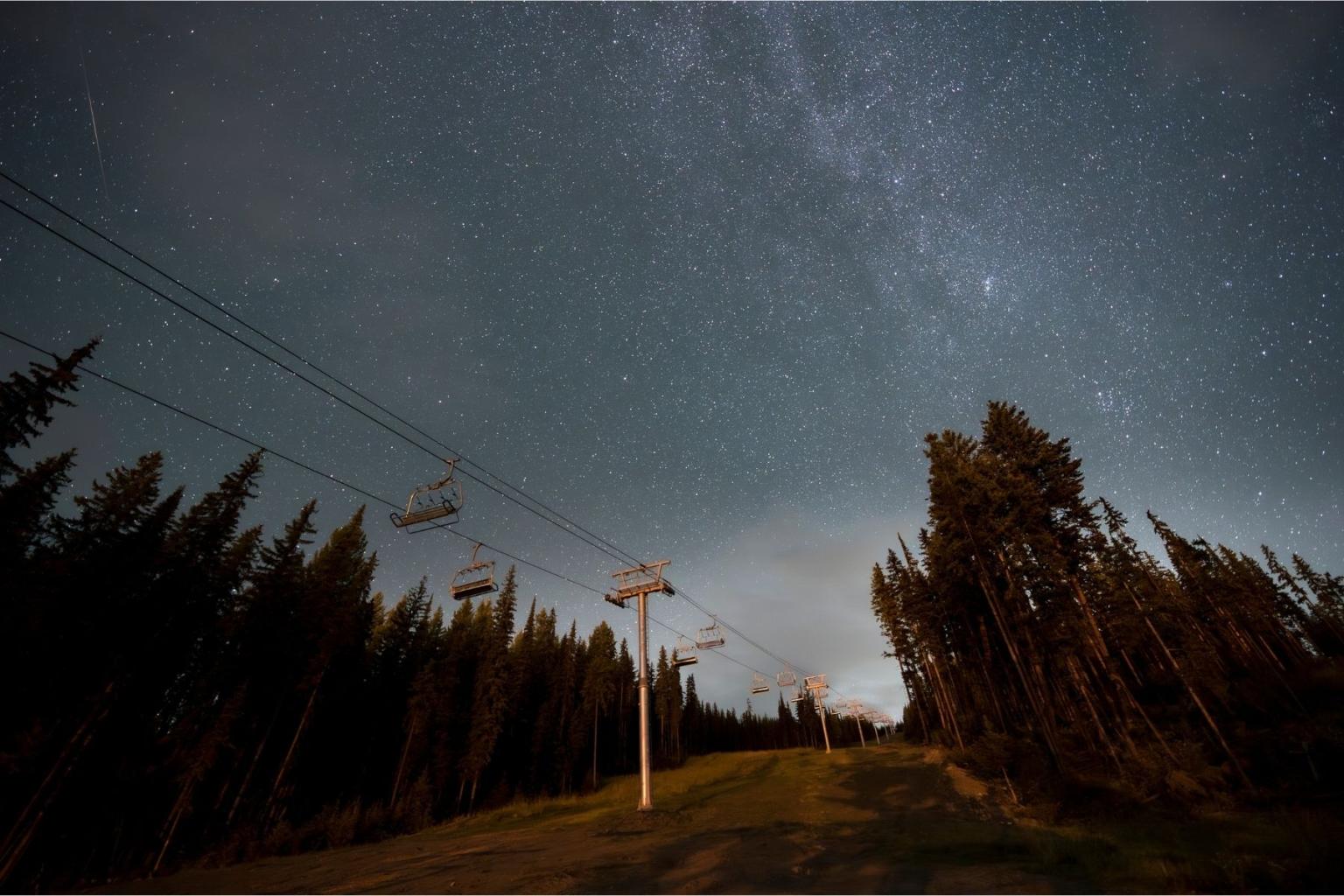 Starry sky over forest and ski lift at night.
