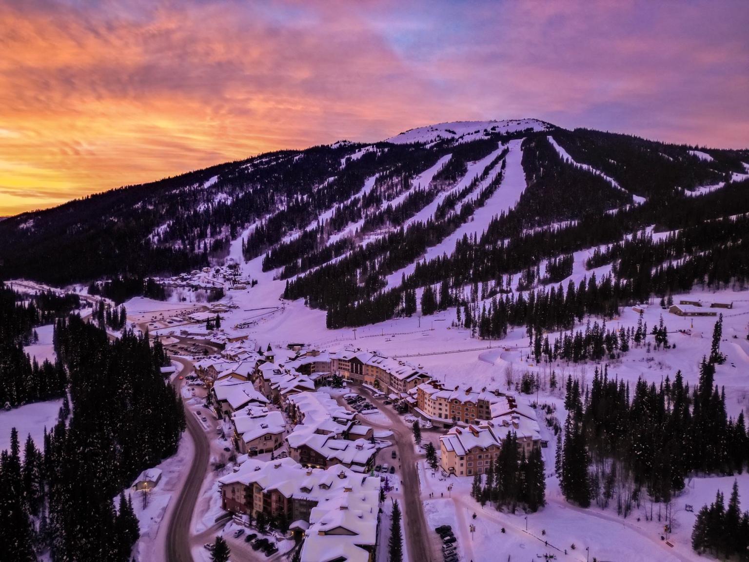 Snowy mountain village at sunset with ski slopes and a vibrant sky.