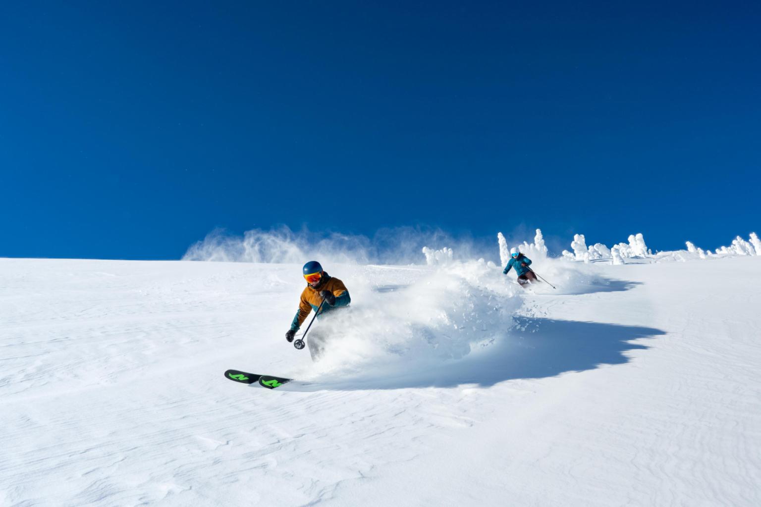 Two skiers on a snowy slope under a clear blue sky.