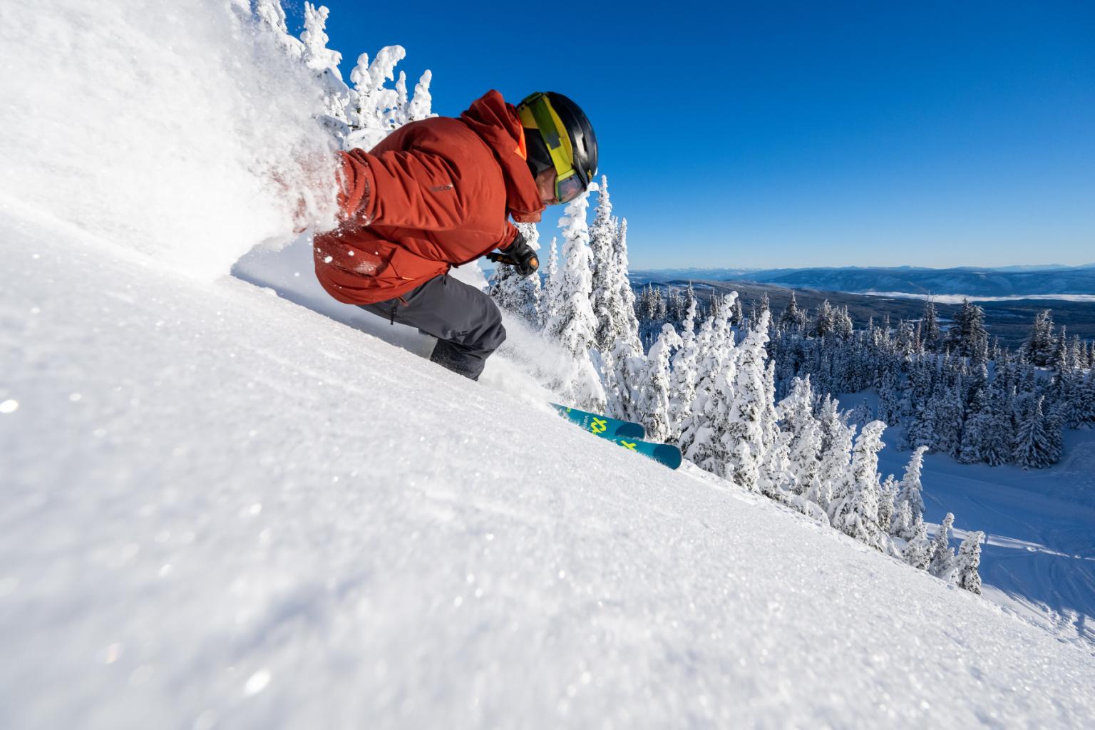 Skier in red jacket navigating snowy slope on clear day.