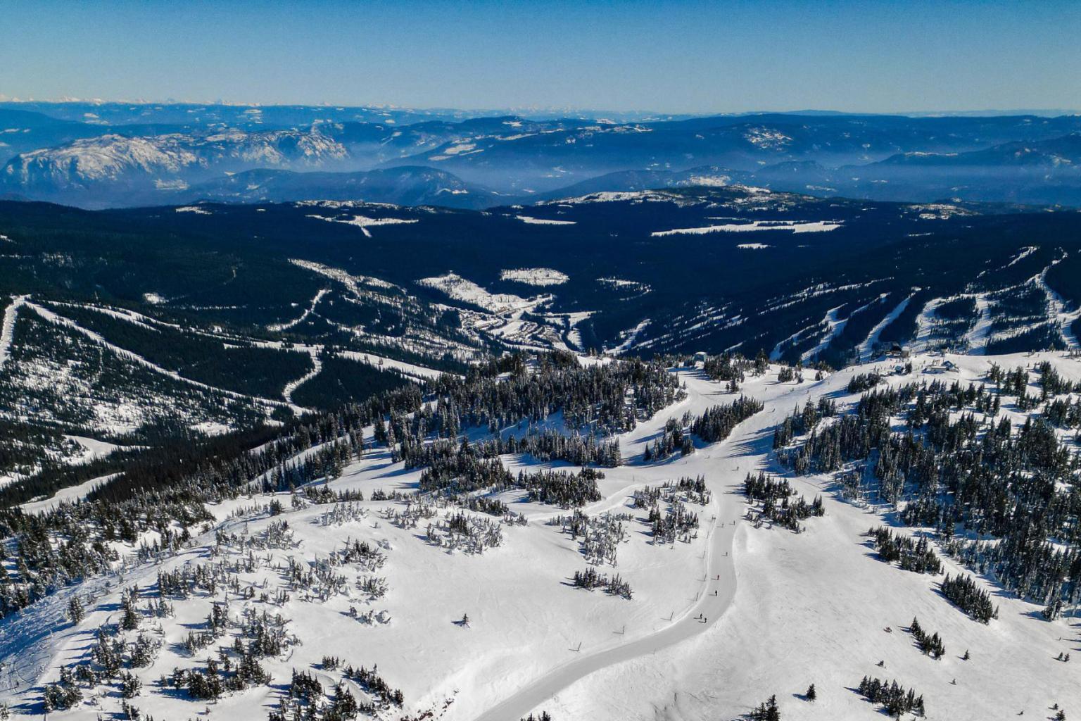 Snowy mountain landscape with ski trails under a clear blue sky.
