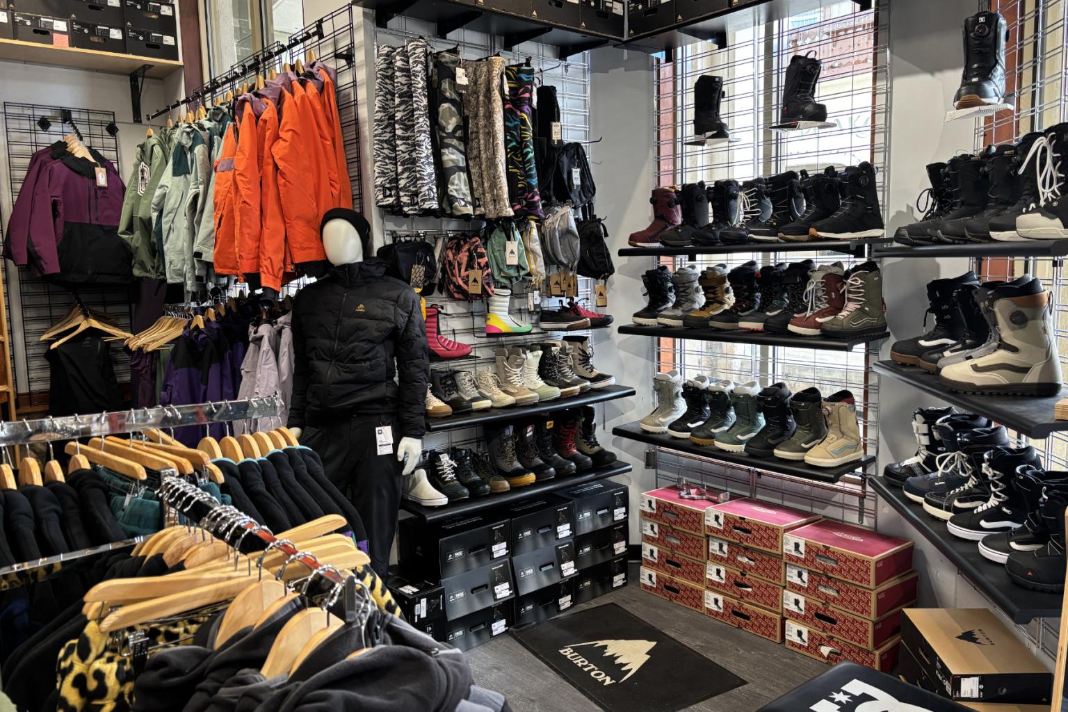 Clothing store interior with jackets, shoes, and snowboard boots on display.