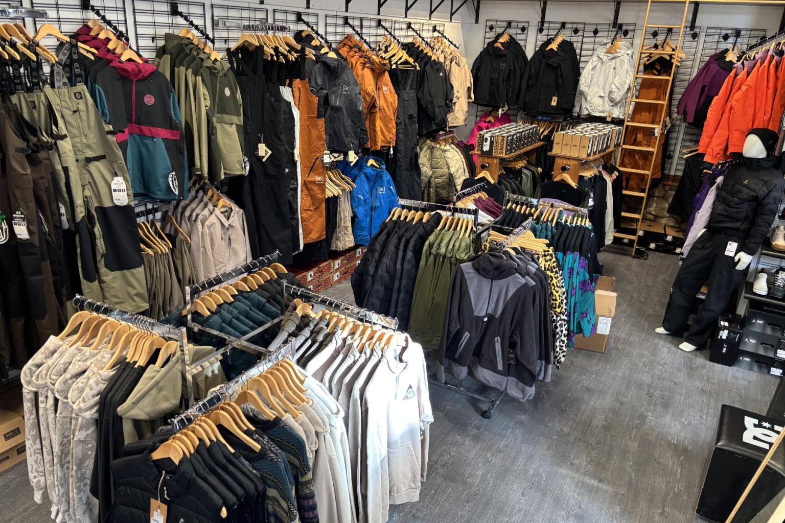 Clothing store interior with colorful jackets and pants on racks.