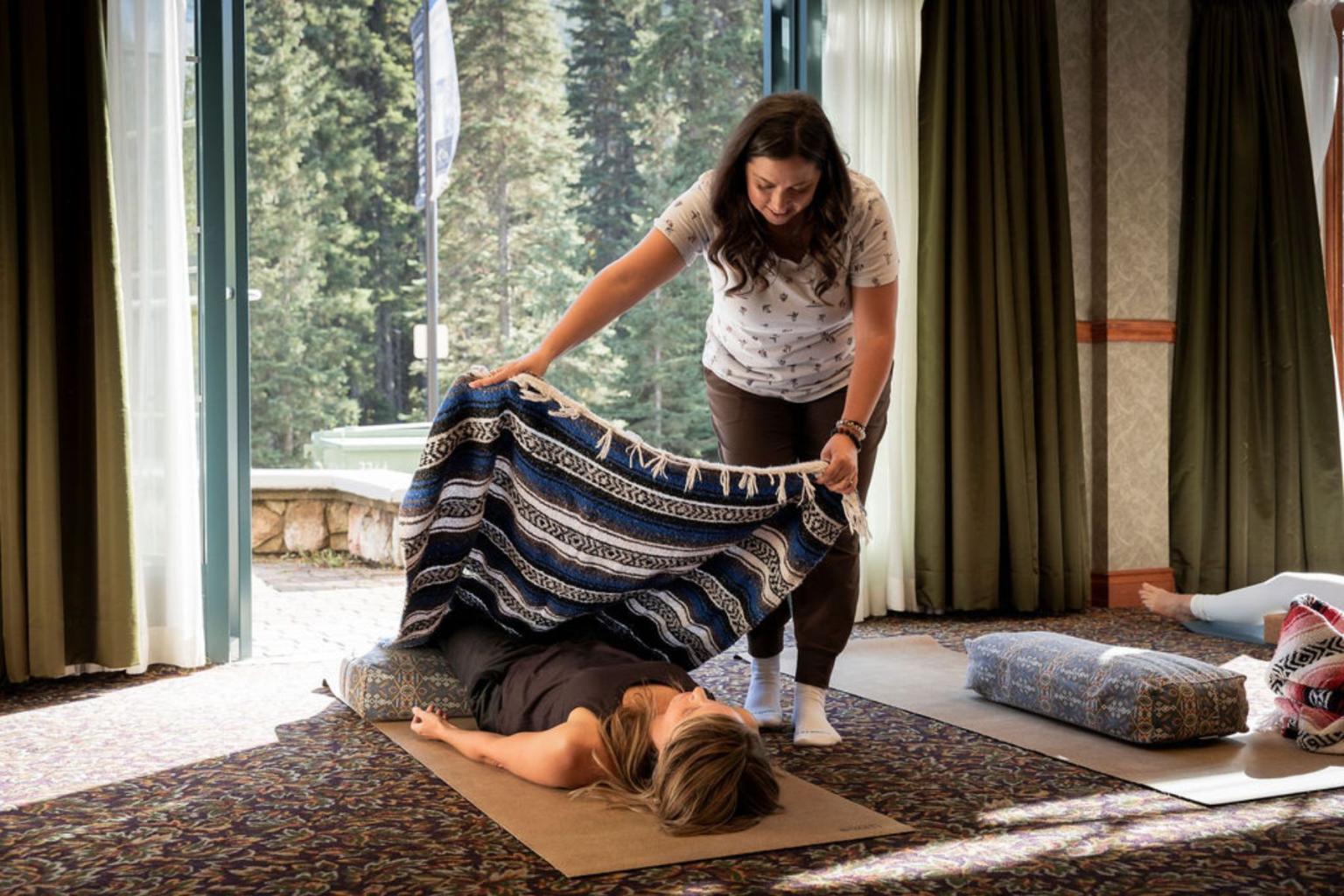 Woman covering another with a blanket in a serene indoor setting.