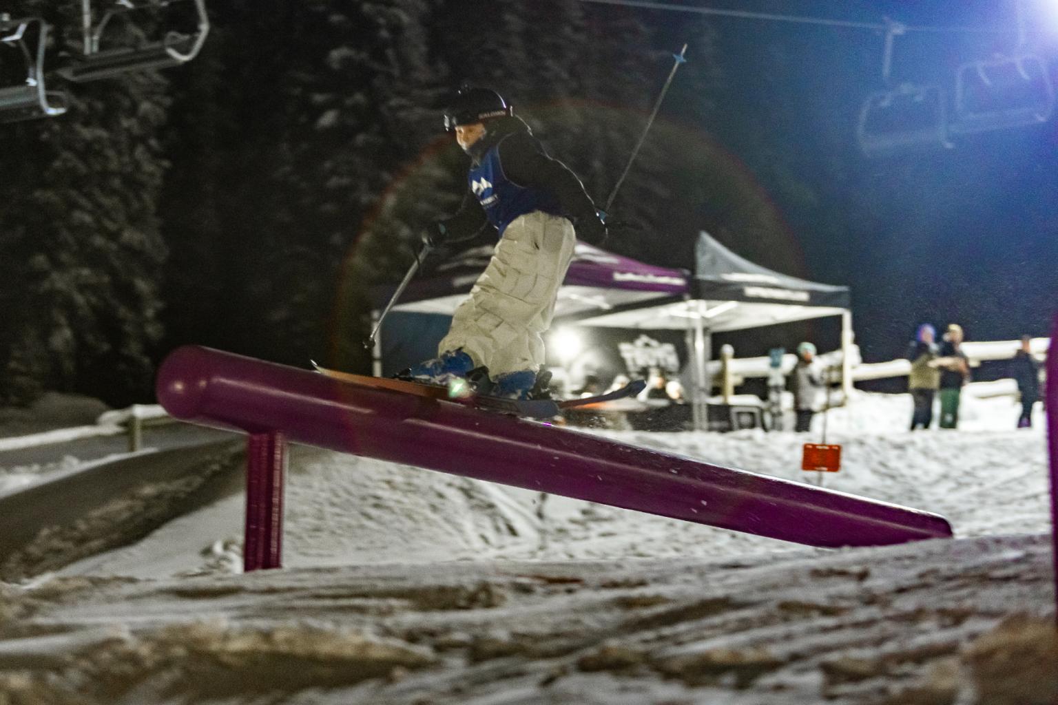 Snowboarder sliding on a rail at night with spectators nearby.