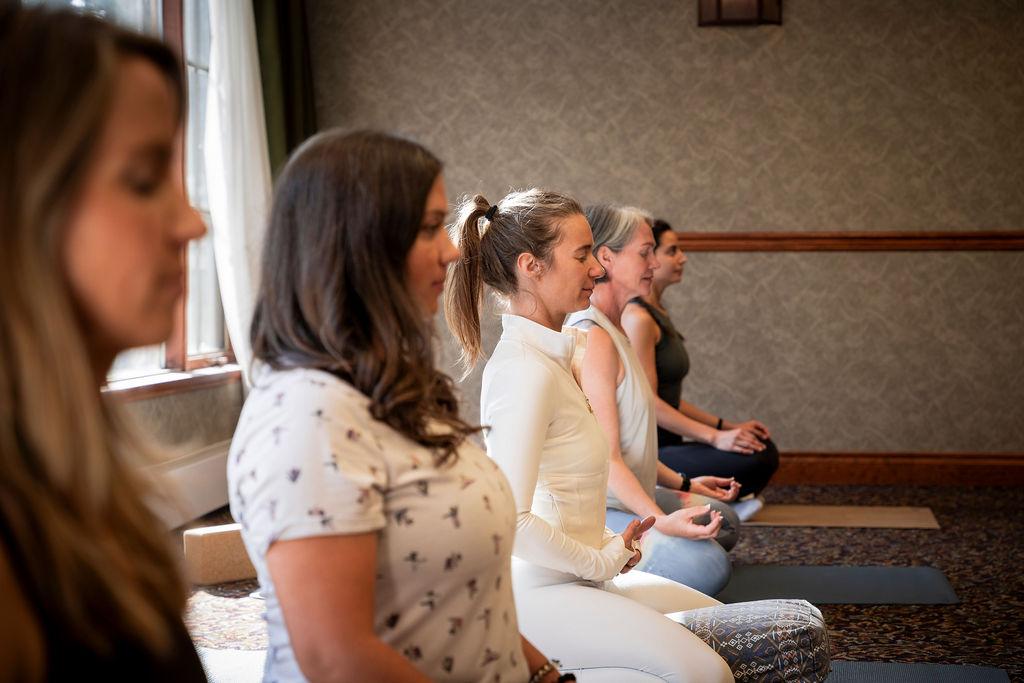 Women sitting cross-legged, meditating indoors.