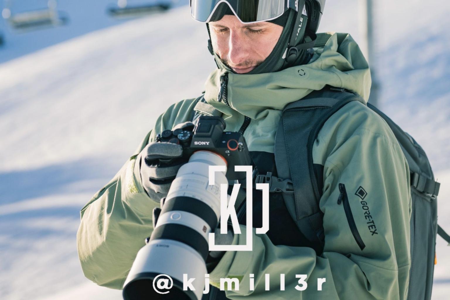 Person in ski gear holding a camera with a large lens on a snowy slope.