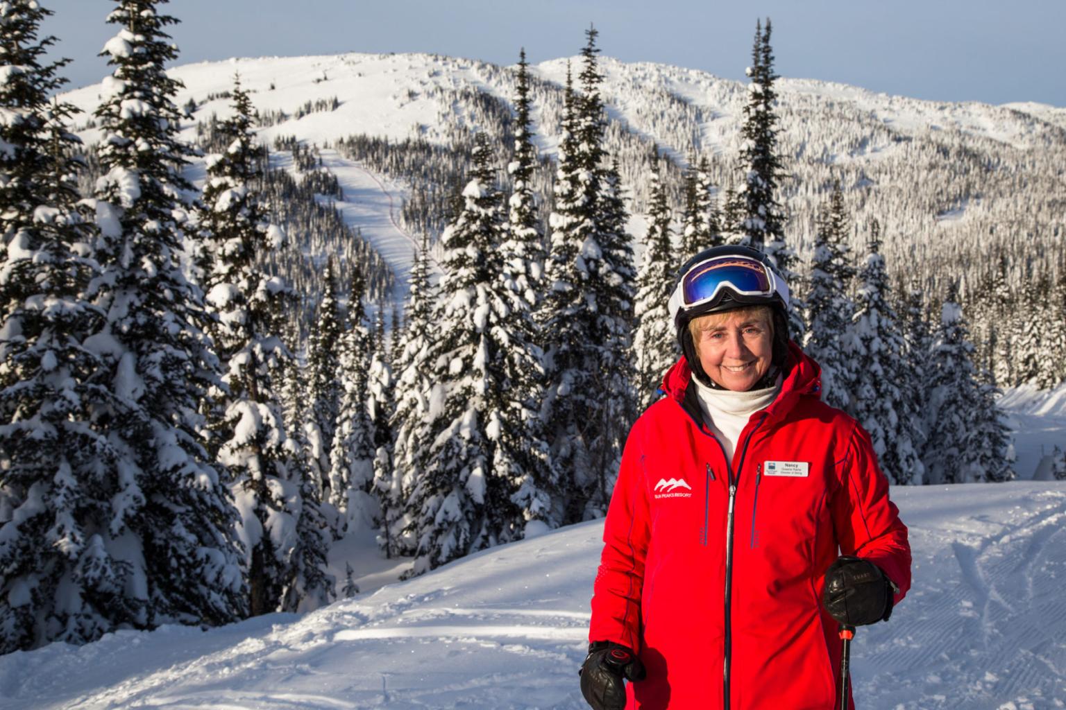 Olympic Champion Skier, Nancy Greene, in red ski jacket, snowy landscape background.
