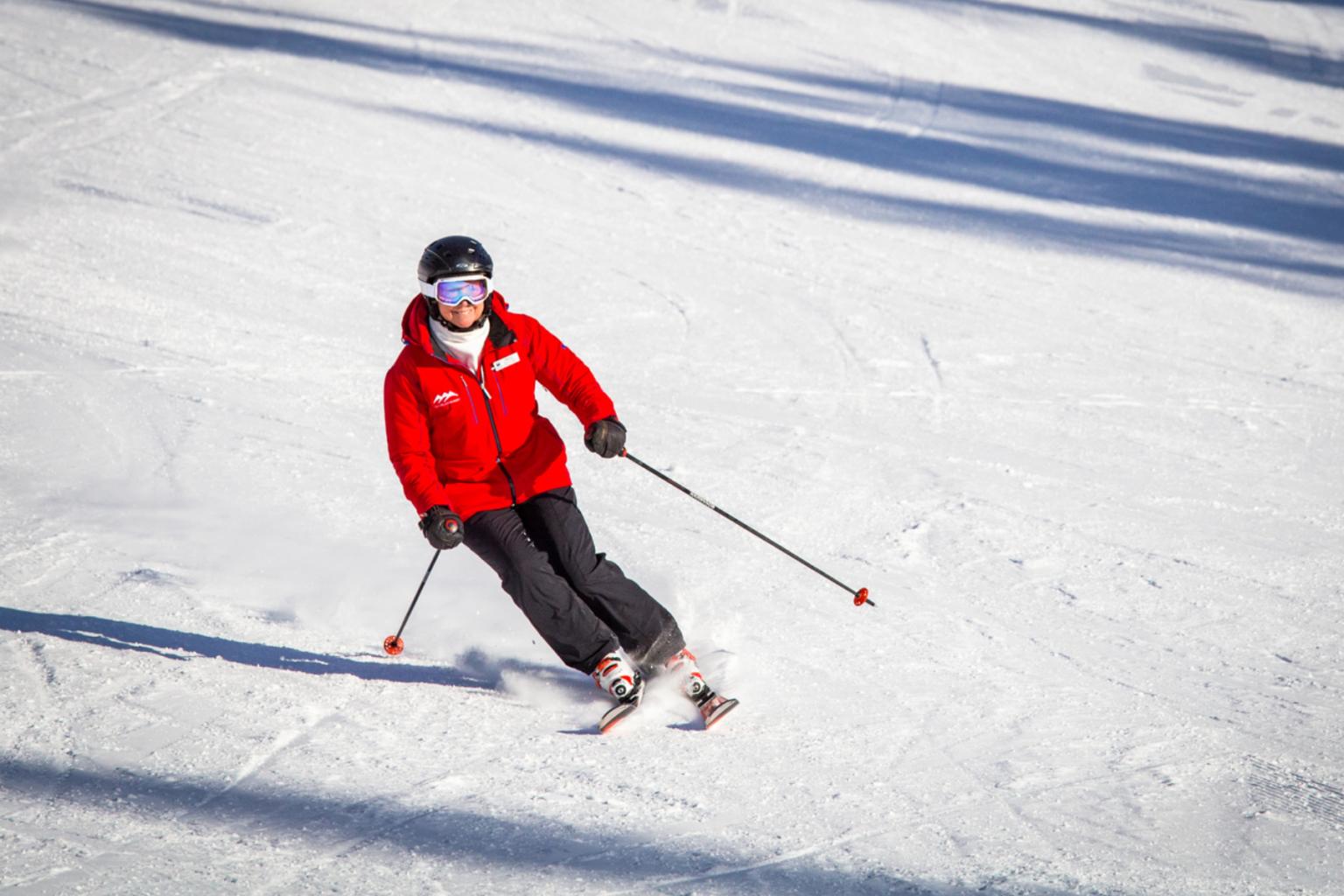 Skier in a red jacket skiing downhill on a snowy slope.