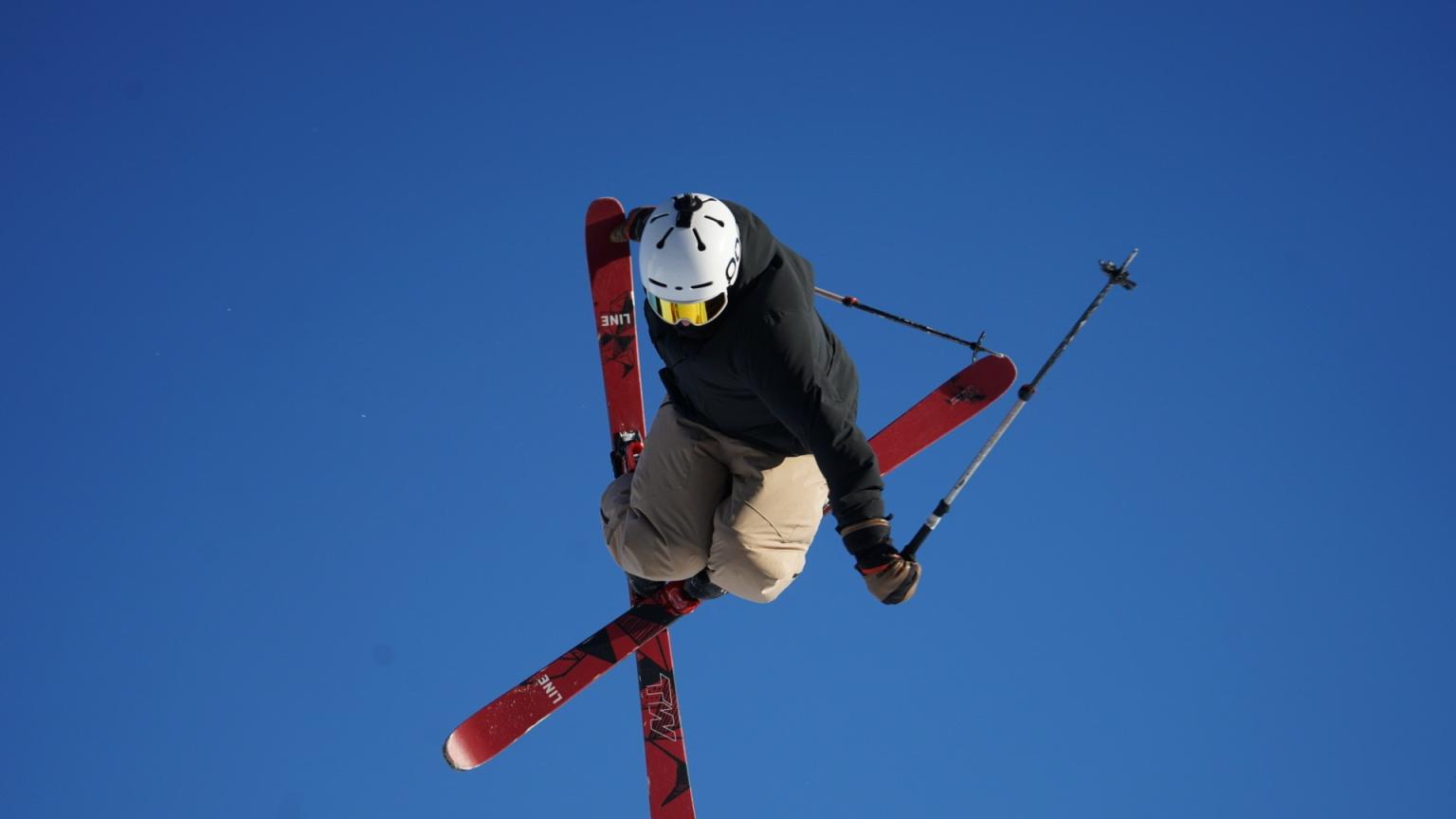 Skier mid-jump with crossed skis against a clear blue sky.
