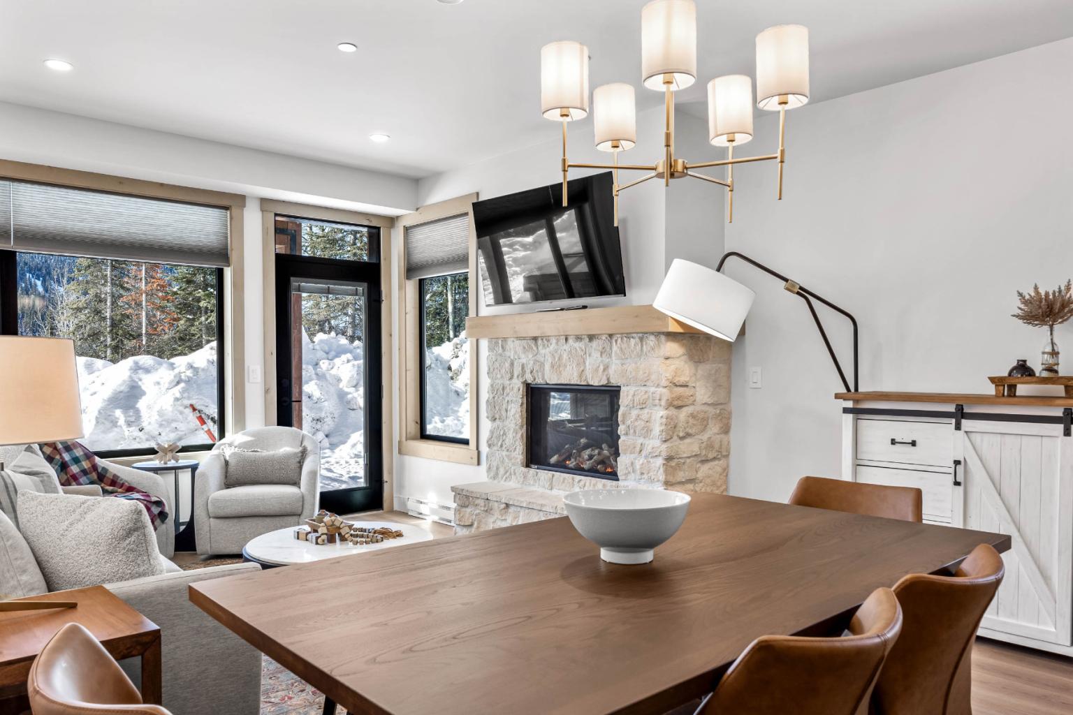 A cozy living room in the Switchback Creek condo features a fireplace, modern furniture, and large windows overlooking the snow.