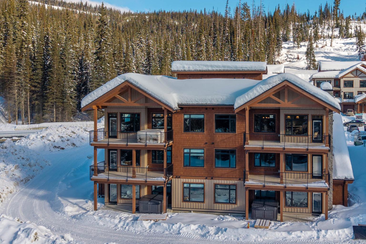 Snow-covered lodge surrounded by pine trees and hills.