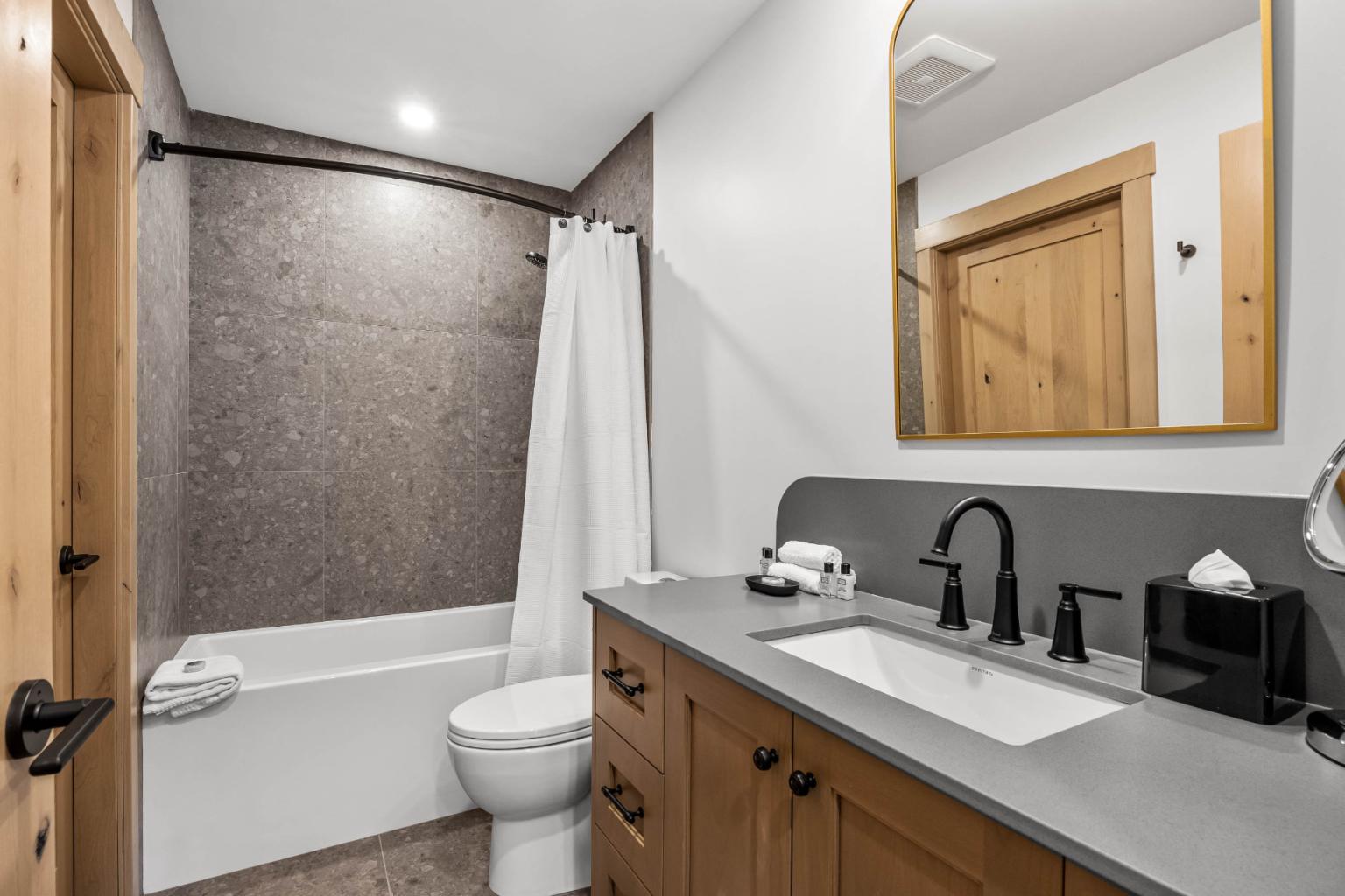 A modern bathroom in the Switchback Creek condo features wooden accents, a white sink, black fixtures, and a bathtub with a curtain.