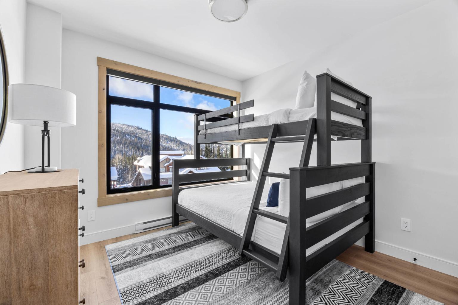 A modern bedroom in the Switchback Creek townhome features black bunk beds, a wood dresser, and mountain views.