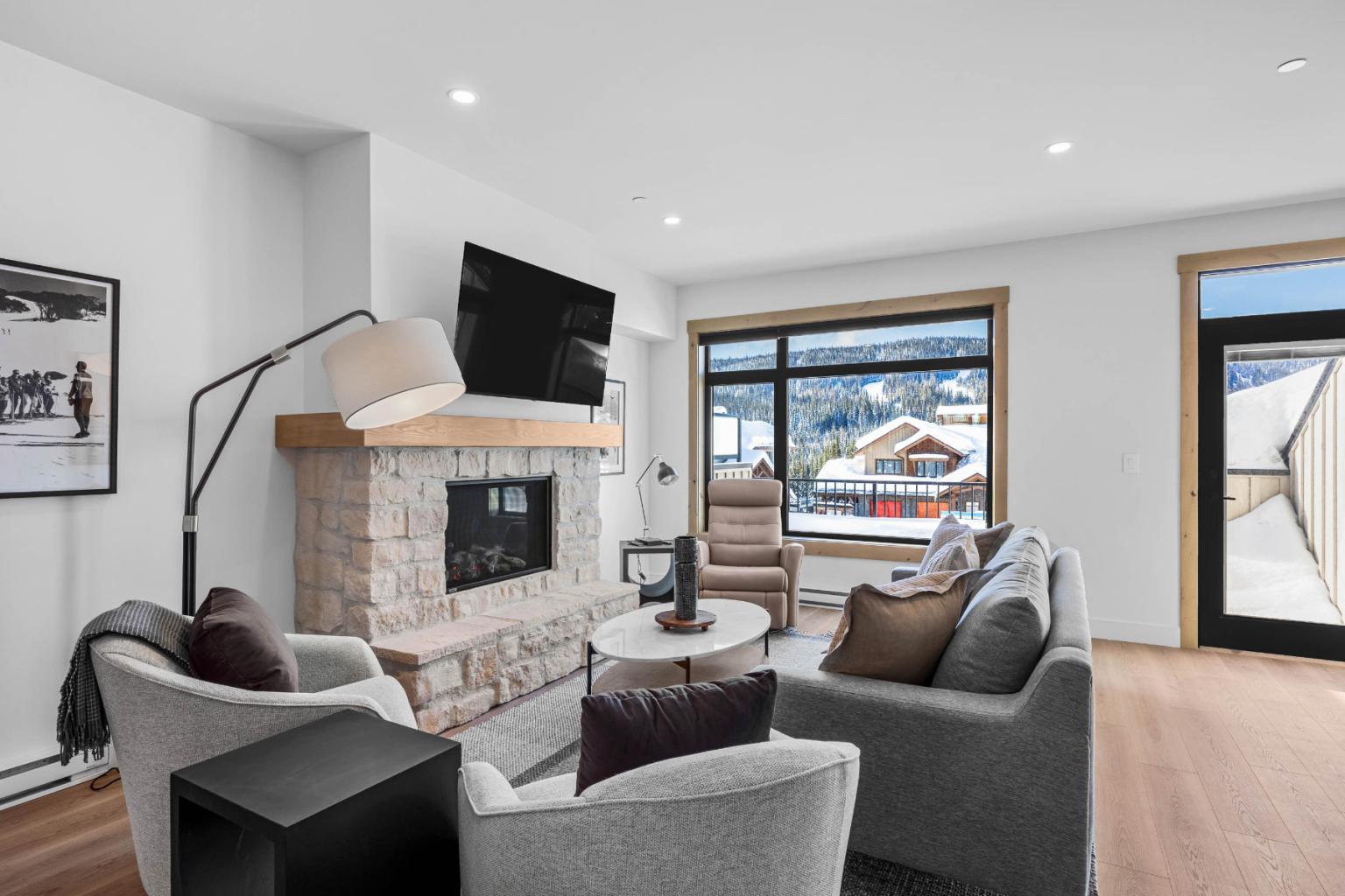 A modern living room in the Switchback Creek townhome features grey furniture, a stone fireplace, and large windows with mountain views.