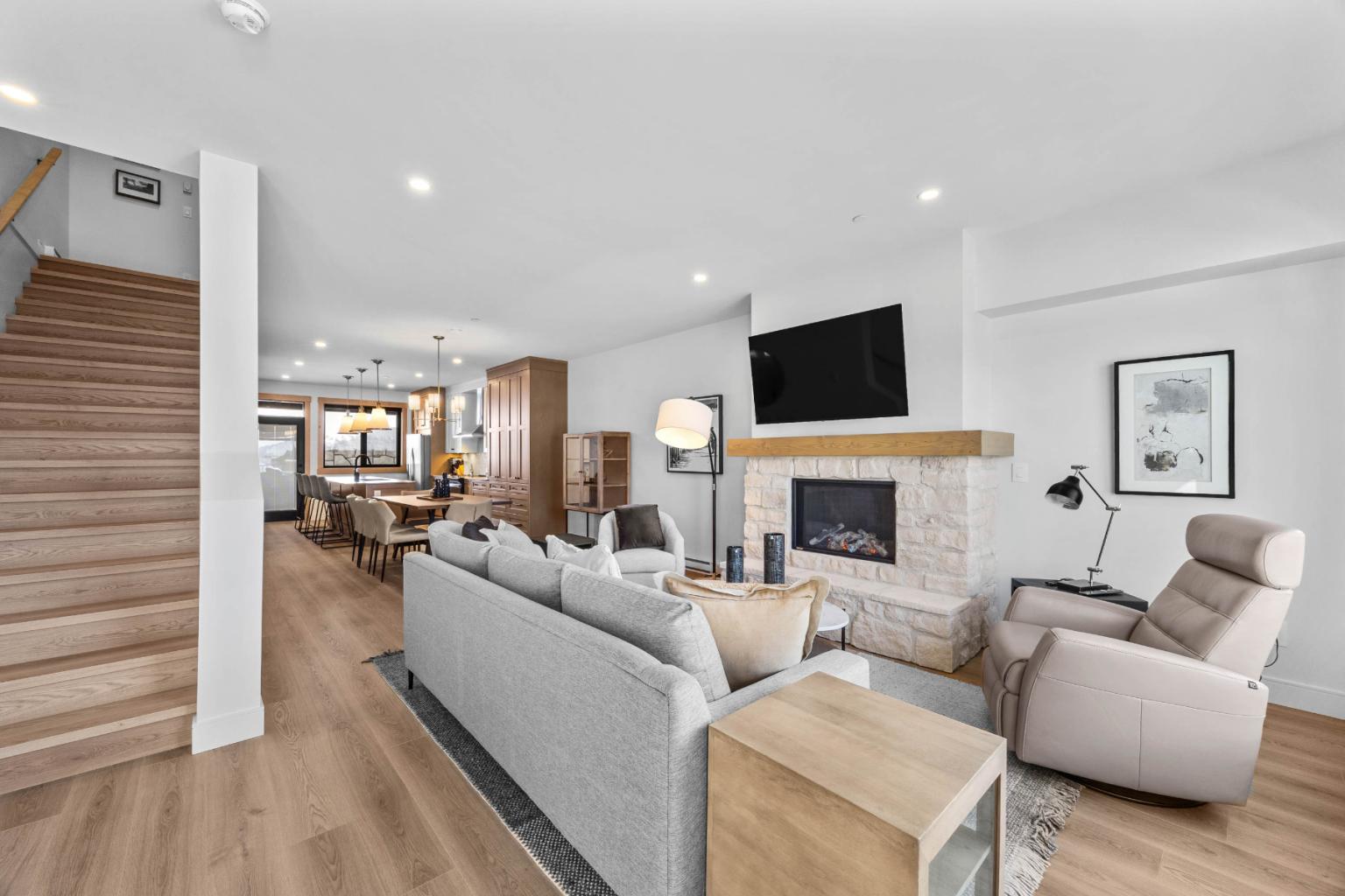 A modern living room in the Switchback Creek townhome features grey furniture, a fireplace, a TV, and wooden floors.