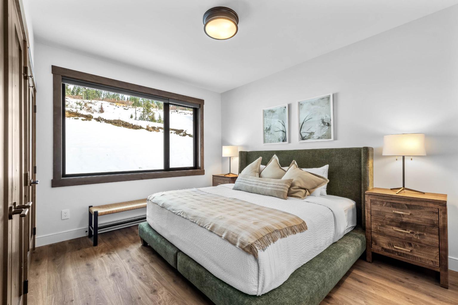 A cozy bedroom in the Switchback Creek townhome features a large bed, two lamps, and a snowy view through the window.