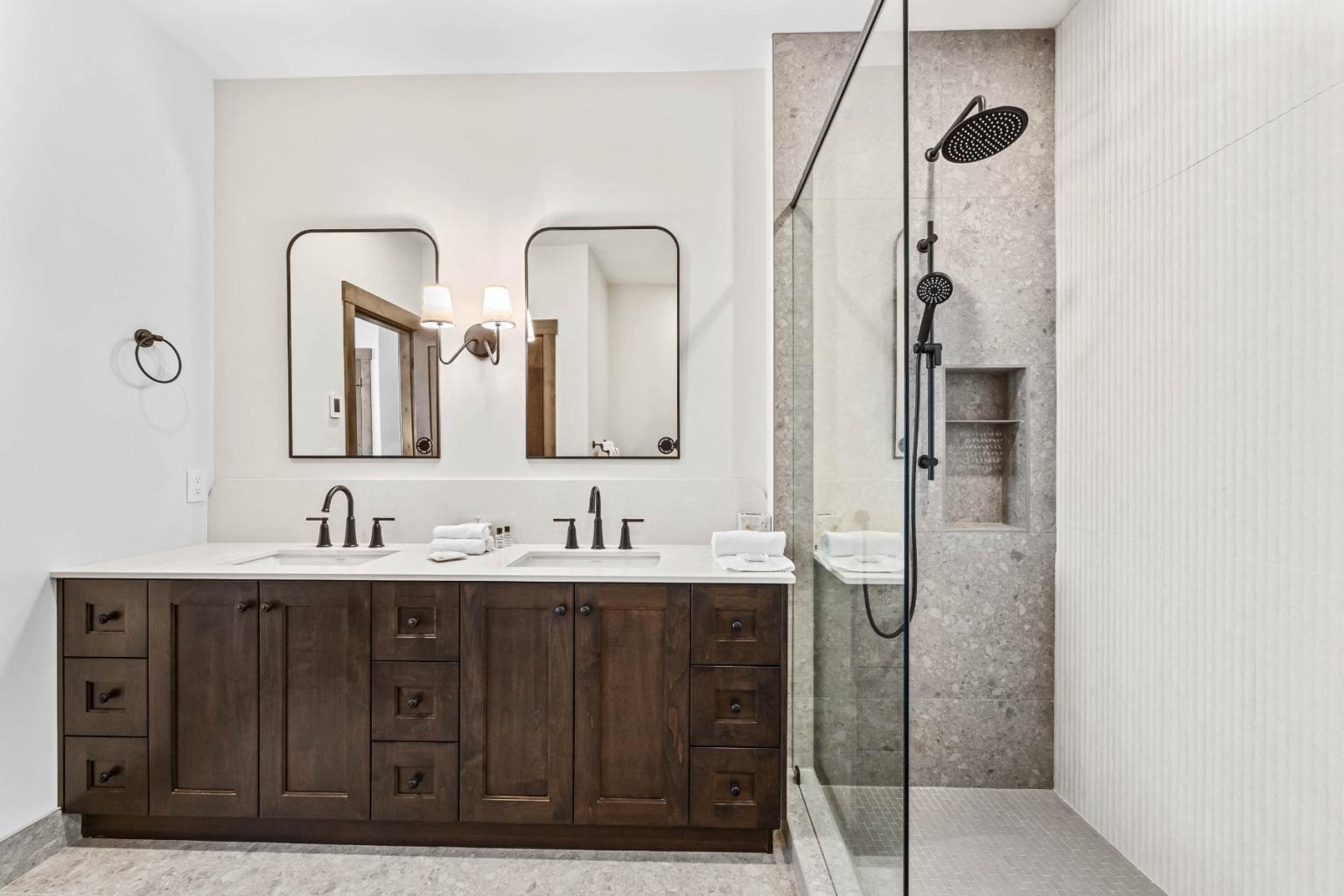 A modern bathroom in the Switchback Creek townhome features a wooden vanity with dual sinks, mirrors, and a glass shower.