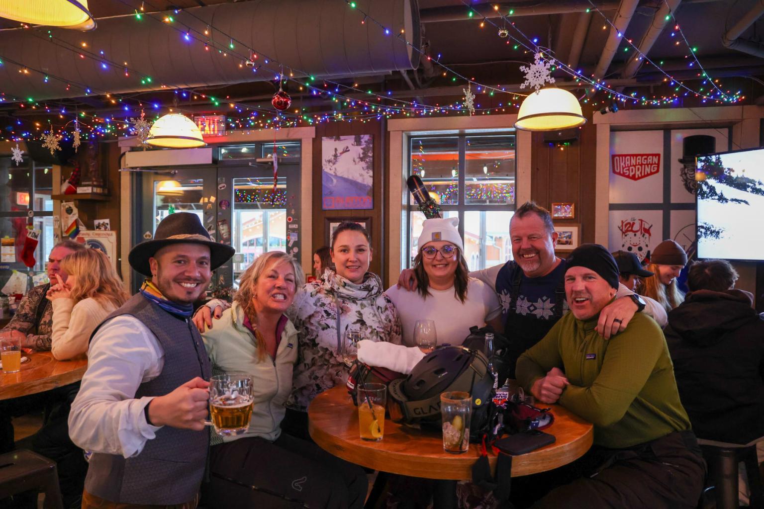 Friends smiling at a cozy bar, surrounded by colorful lights and festive decor.