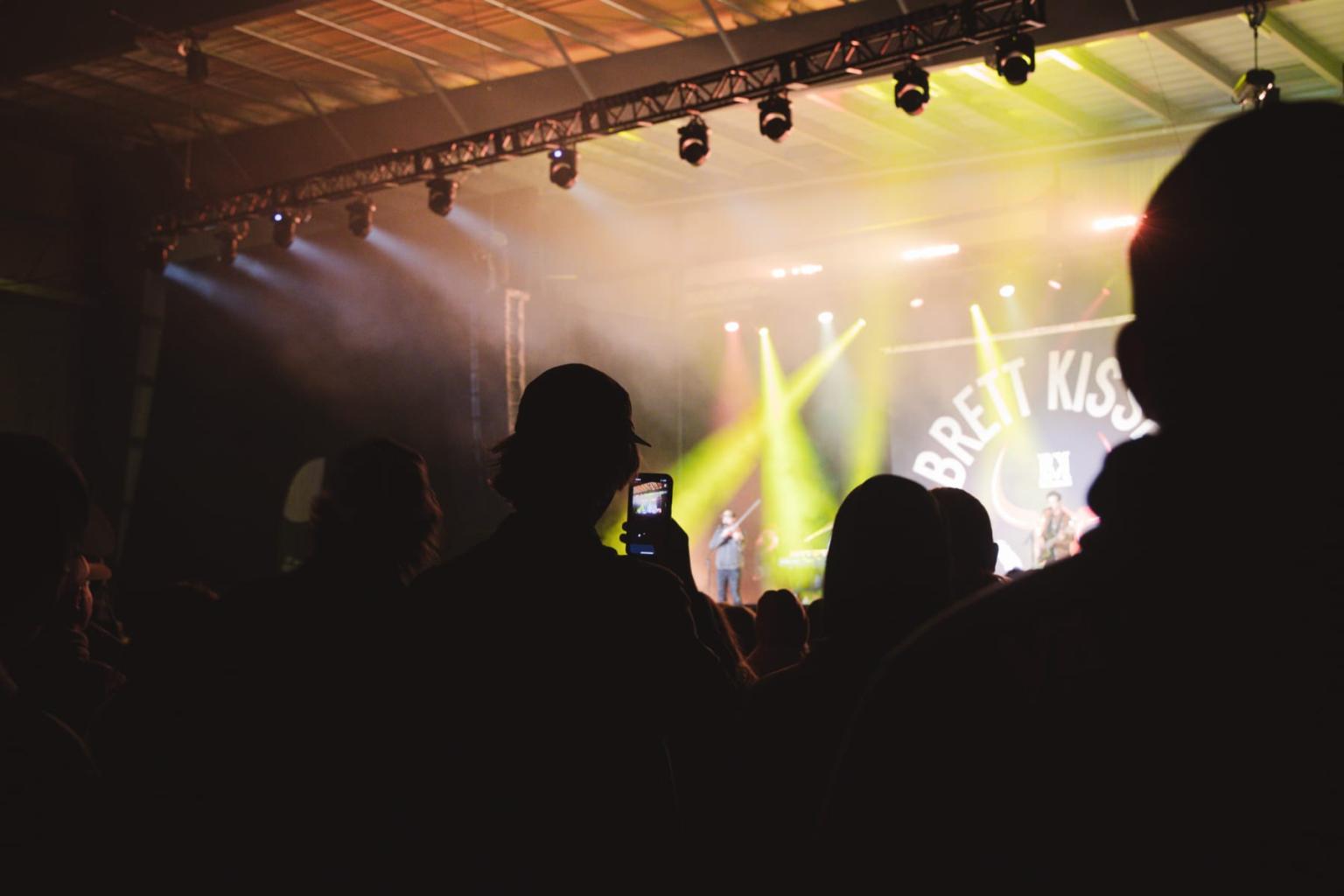 Concert audience in silhouette, stage with bright lights in the background.