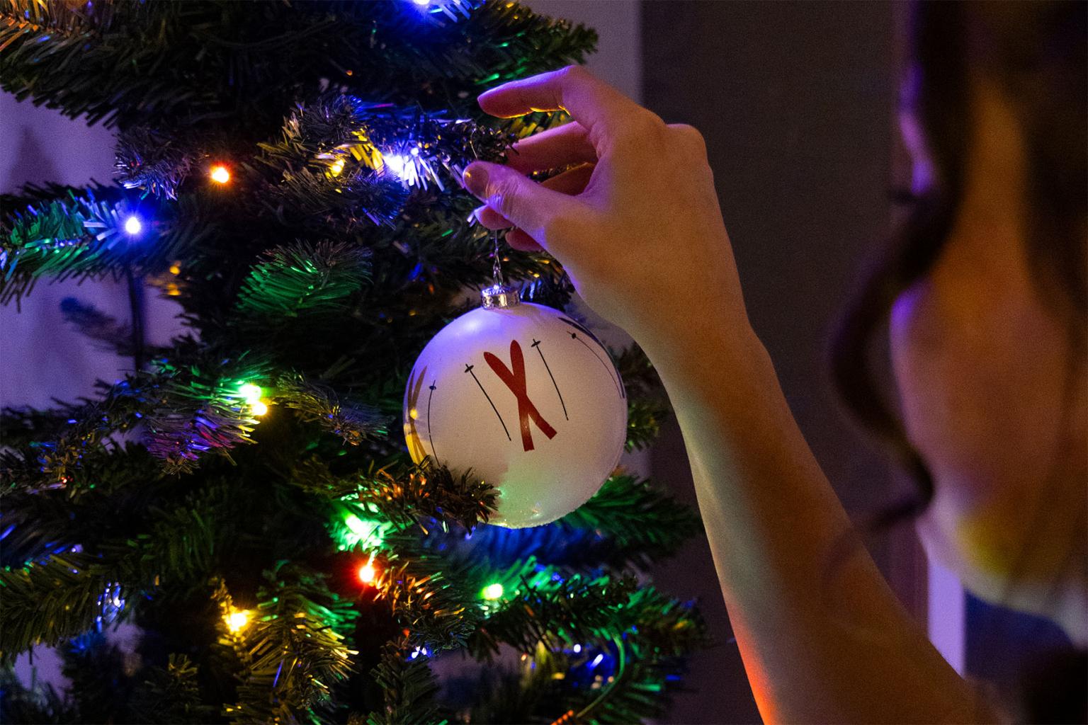 Hand placing ornament on a lit Christmas tree.