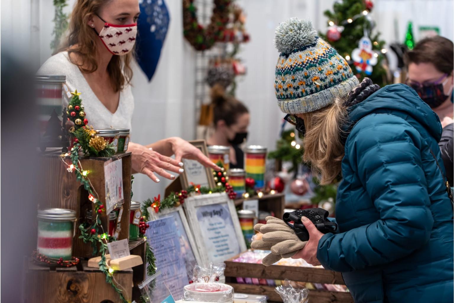 Woman in mask and a customer at a holiday market booth.