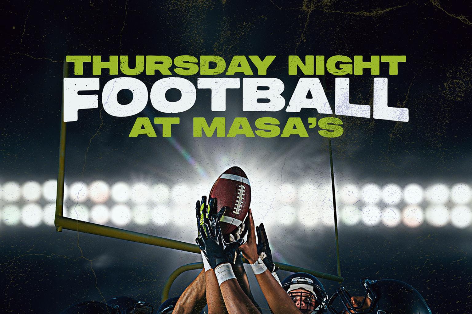 Players reaching for a football under stadium lights.