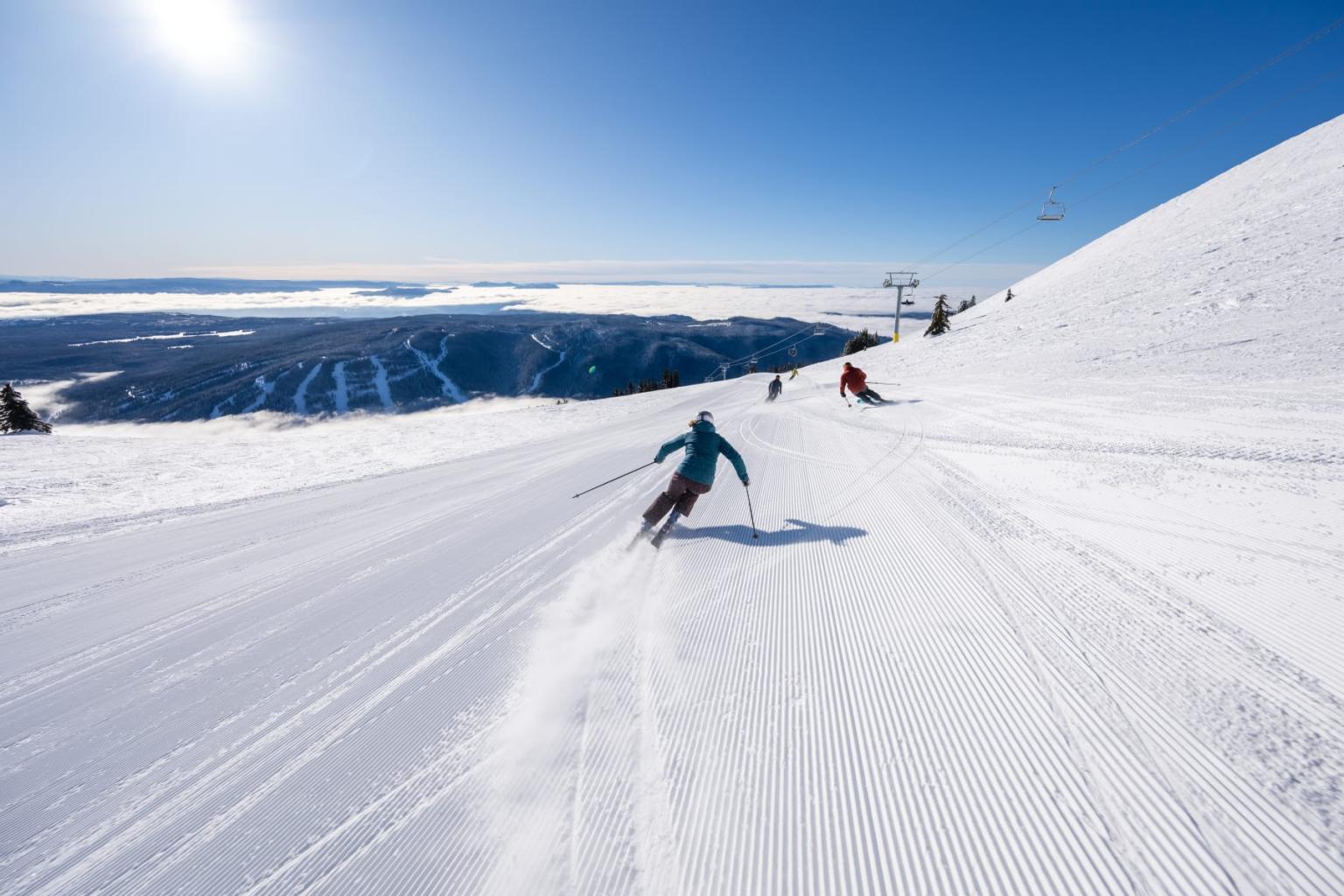 Skiers glide down a snowy slope under a clear blue sky.