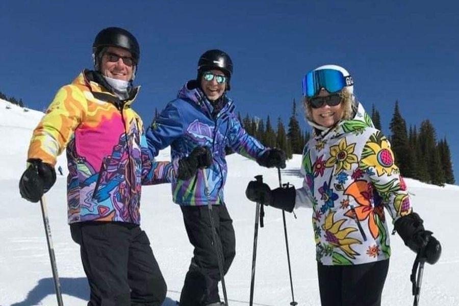 Three people in colorful ski jackets smiling on a snowy slope under a clear blue sky.