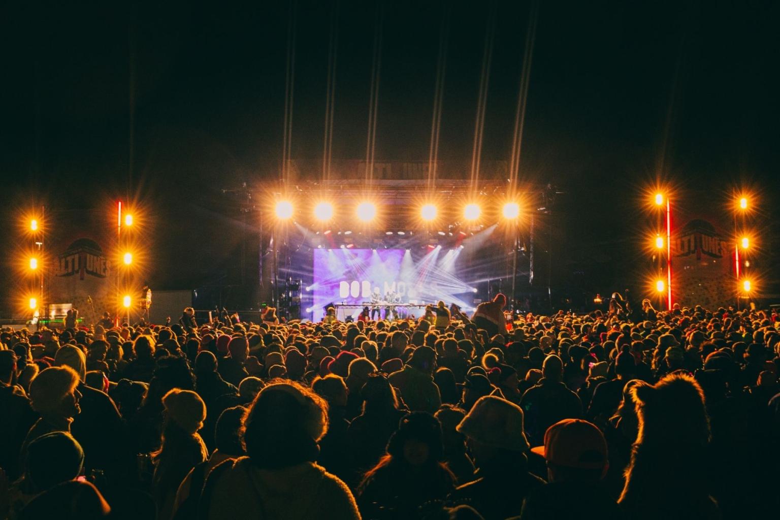 Crowd at night concert, stage lit with bright yellow lights.