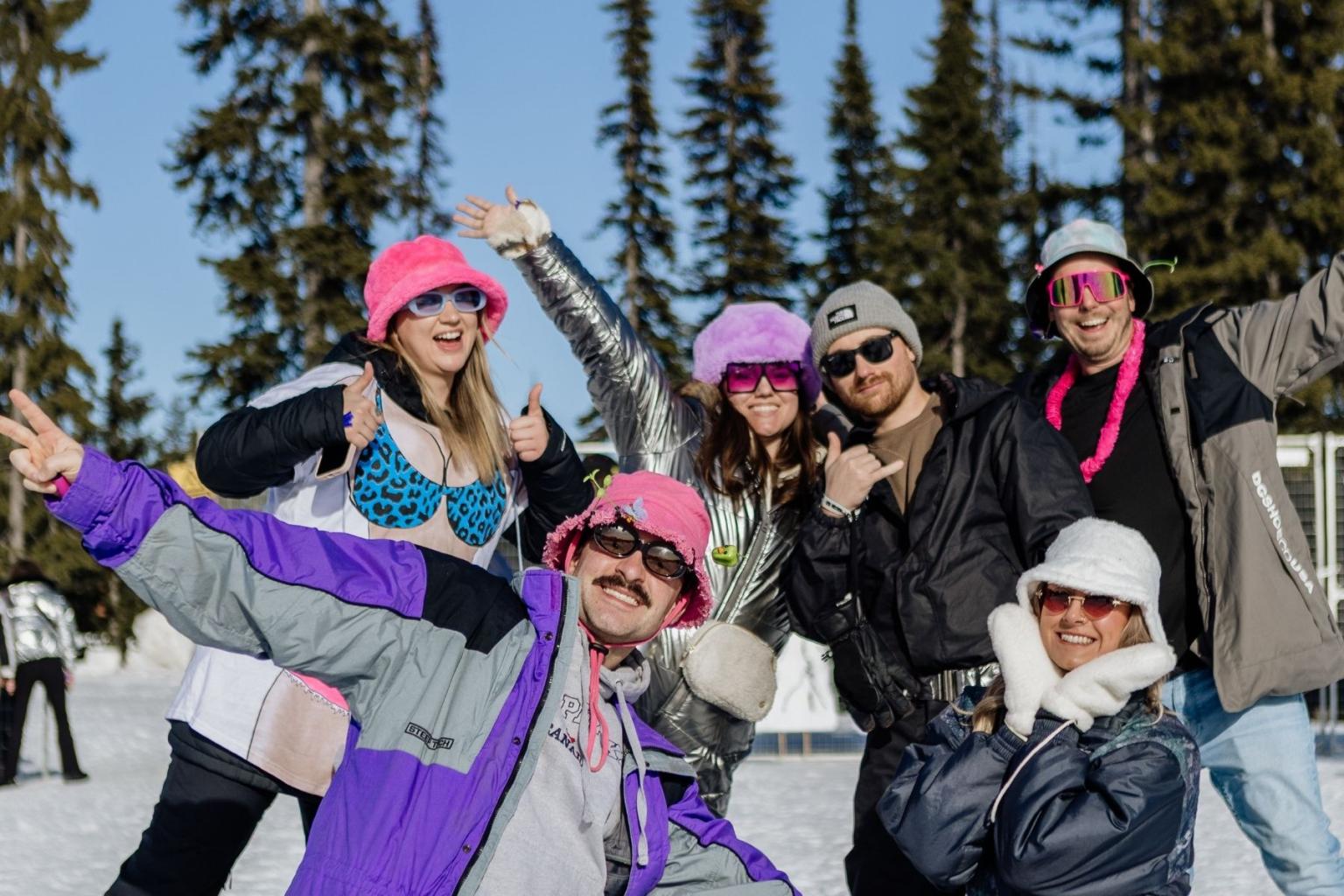 Group of people in colorful winter gear posing in the snow with trees in the background.