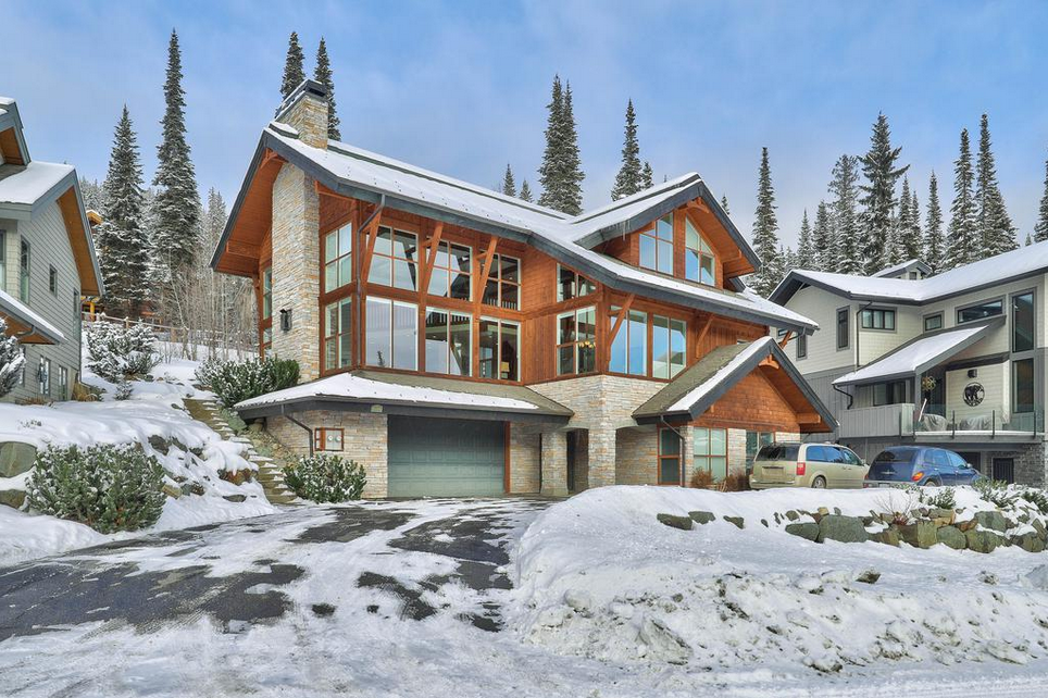 Snow-covered chalet with wooden accents and tall conifer trees.