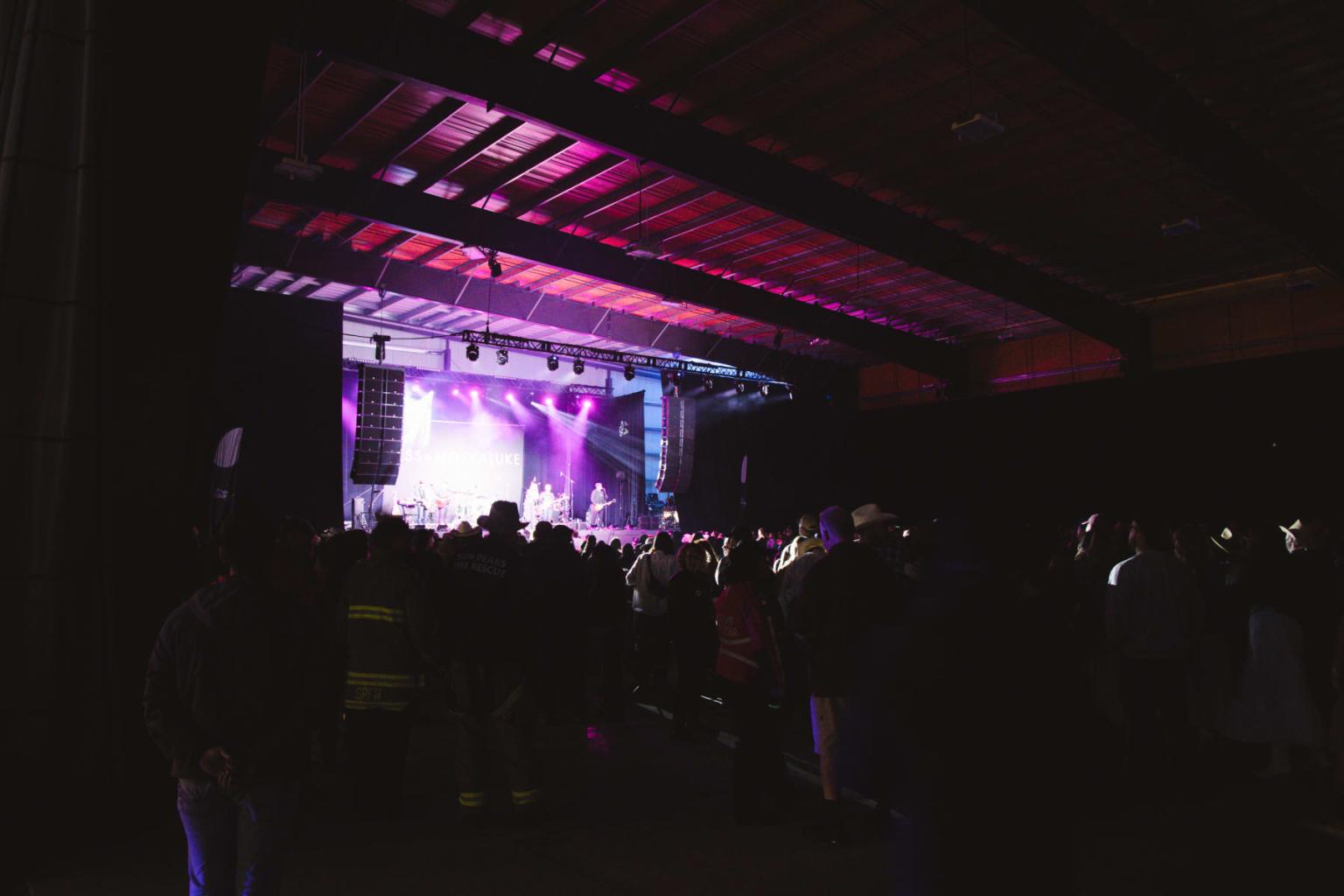 Crowd in a dimly lit venue watching a stage with purple lights.