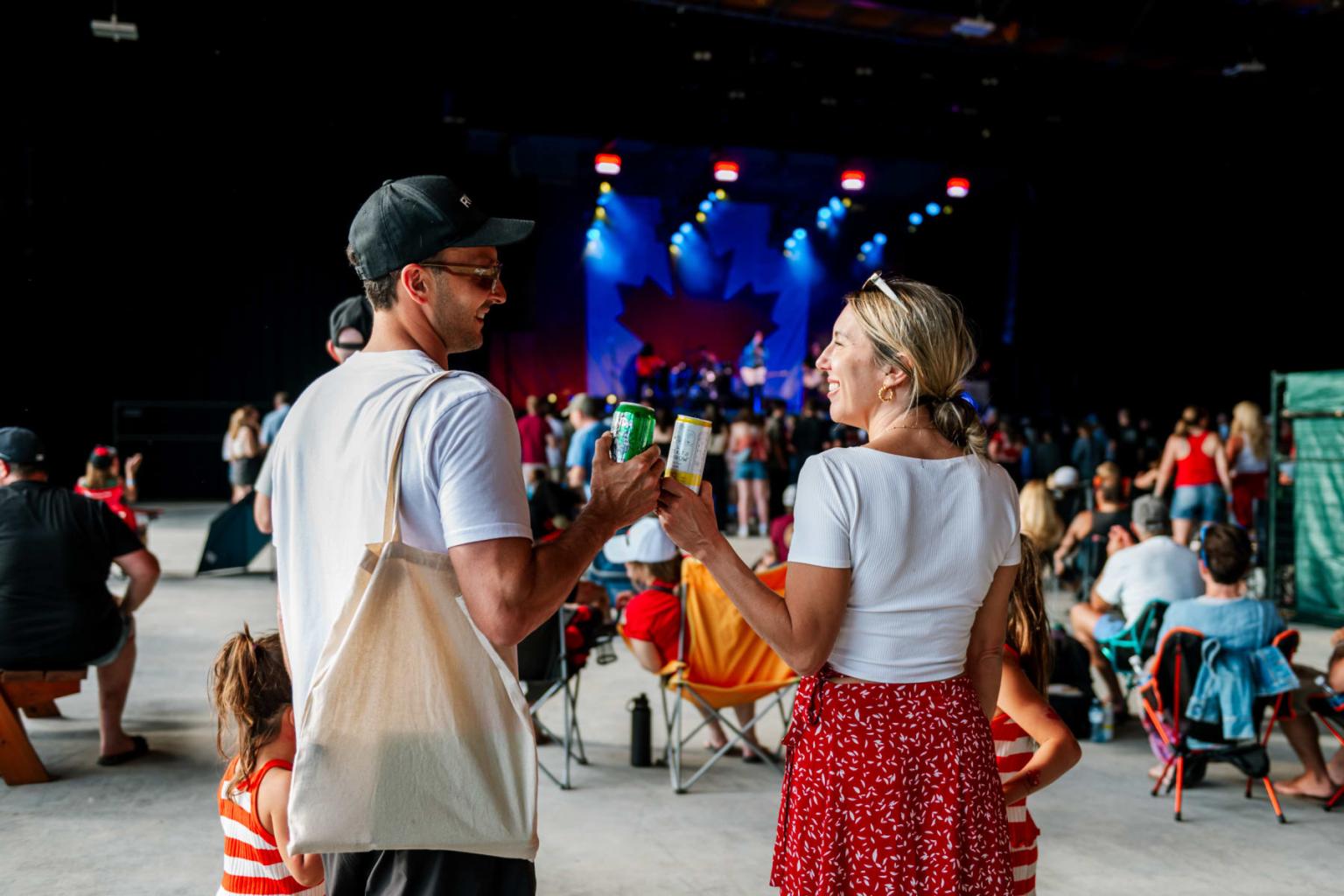 Couple holding hands at outdoor concert, crowd watching stage.